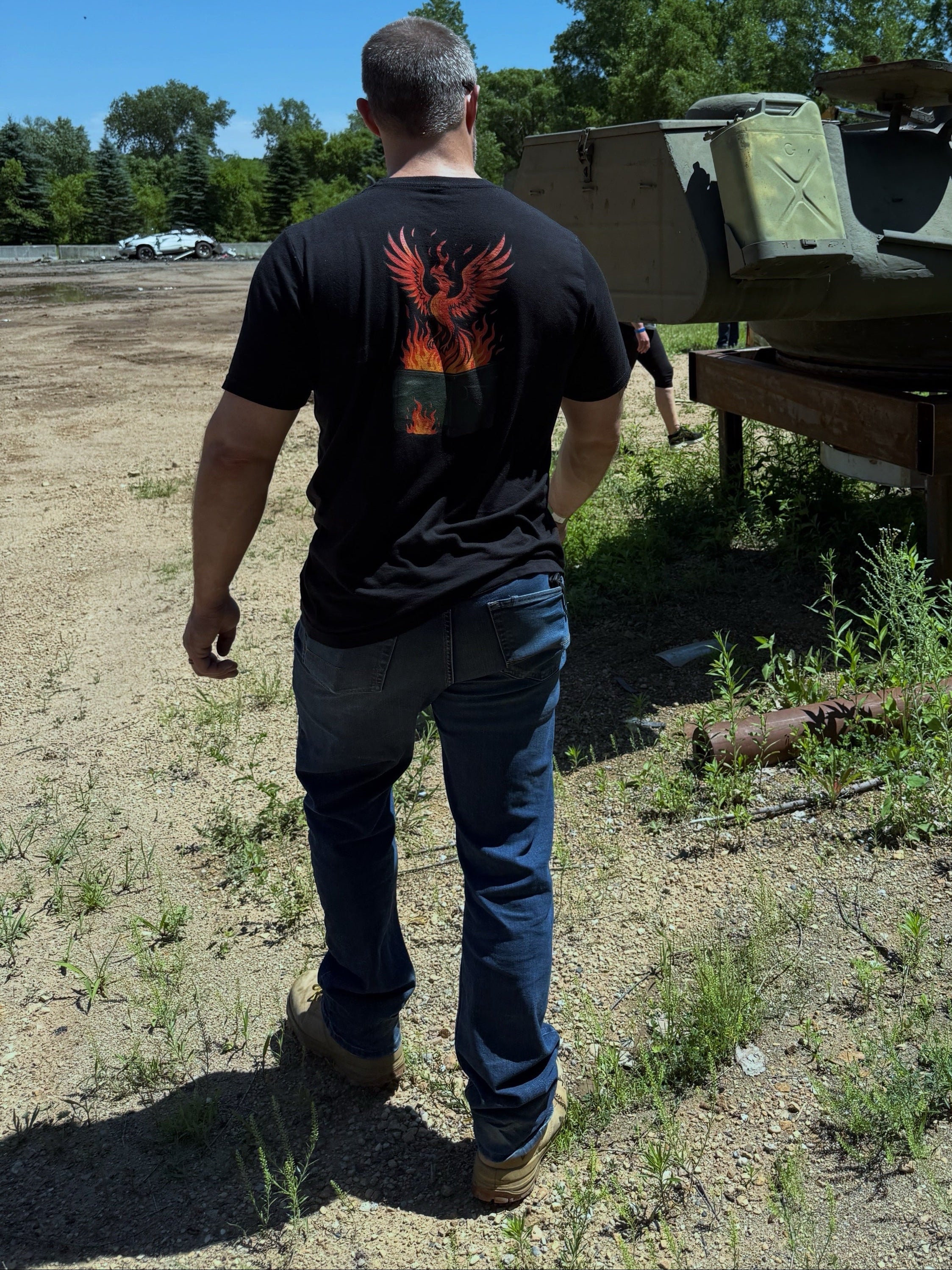 Man standing next to an old military vehicle in an open area with trees in the background